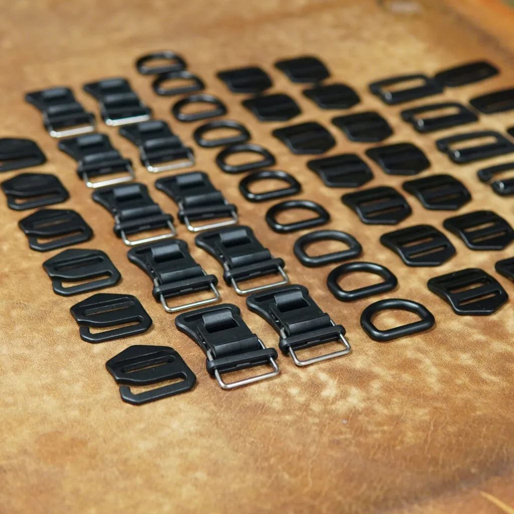 Aluminium buckles, hooks and D-rings for the LUMABAG bags, laid out on leather